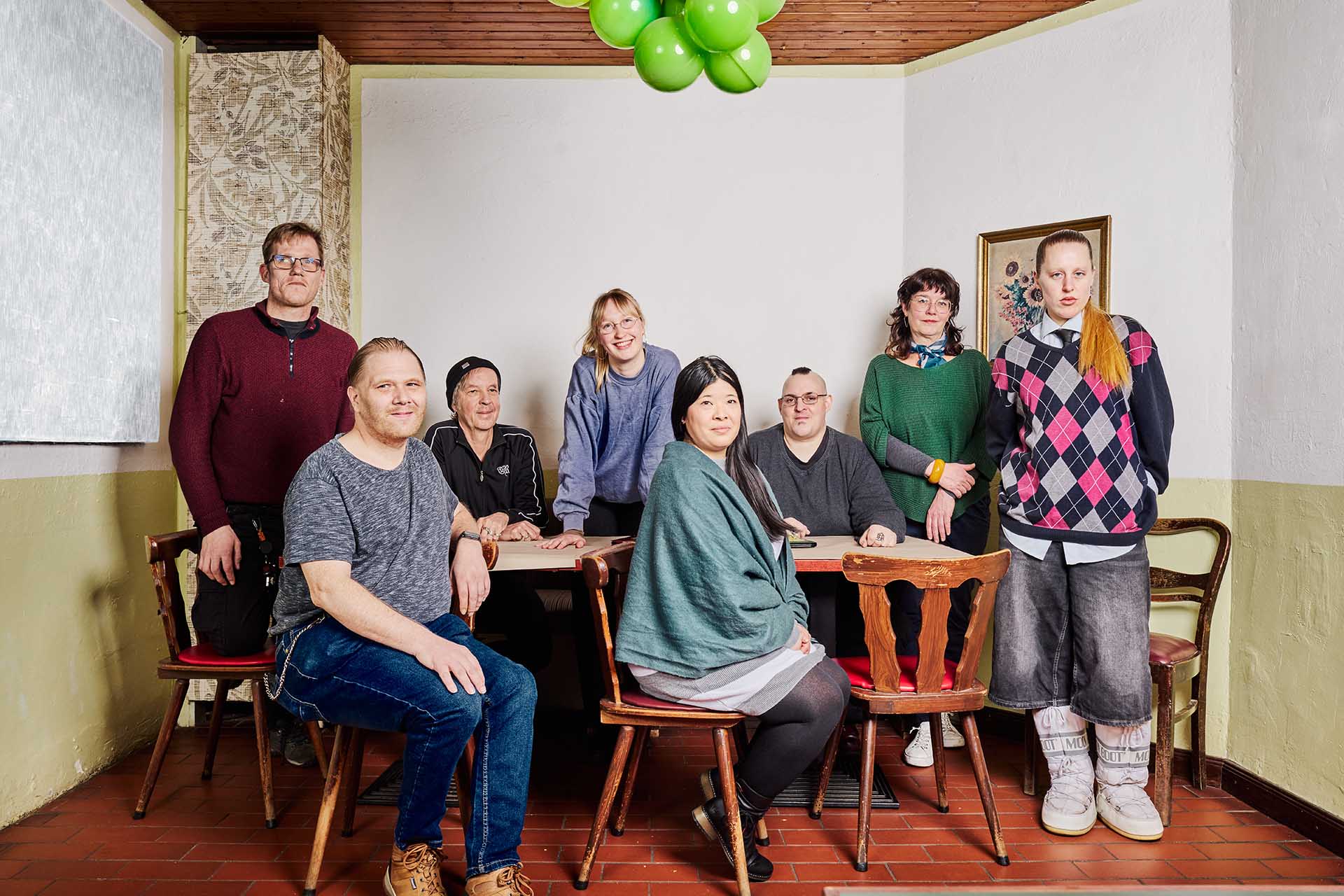 Teamfoto Klappe auf 2025: 8 Personen (4 Frauen und 4 Männer), sitzen um einen Tisch in einem Restaurant. Freundlich schauen sie in die Kamera.